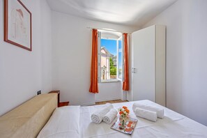 A hotel room with a bed, a window with curtains, a framed artwork on the wall, and a view of buildings outside.