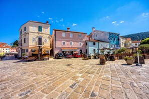 Uma praça de pedra com edifícios históricos, mesas ao ar livre e carros estacionados.