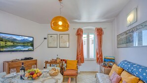 Un comedor con una mesa preparada para cuatro, un sofá, un televisor y obras de arte en las paredes.