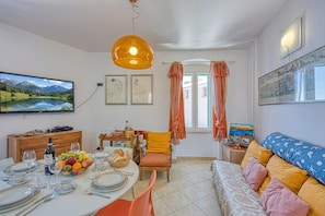 Uma área de refeições com uma mesa posta para quatro pessoas, um sofá, uma televisão e obras de arte nas paredes.