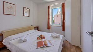 Habitación de hotel con cama, ventana con cortinas, mesita de noche y un cuadro con dos imágenes enmarcadas.