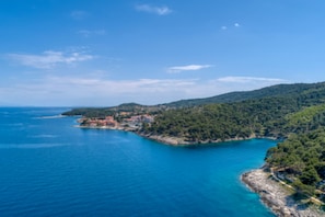 Un paisaje costero con mar azul cristalino, una pequeña península con edificios y una colina boscosa.