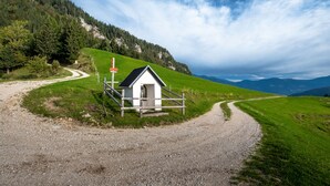 A small white building with a red sign, surrounded by a gravel path and green fields, with mountains in the background. - Kunstek Farmhouse w/ Private Sauna, Rogatec, Slovenia (Rogatec)
