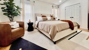 Een moderne slaapkamer met een bed, een bruine leren fauteuil, een potplant en een witte deur.