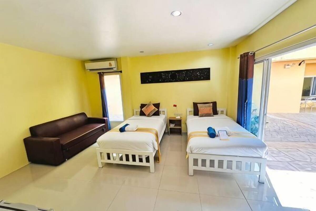 Habitación de hotel con dos camas, un sofá, aire acondicionado instalado en la pared y una puerta corrediza de vidrio al exterior.