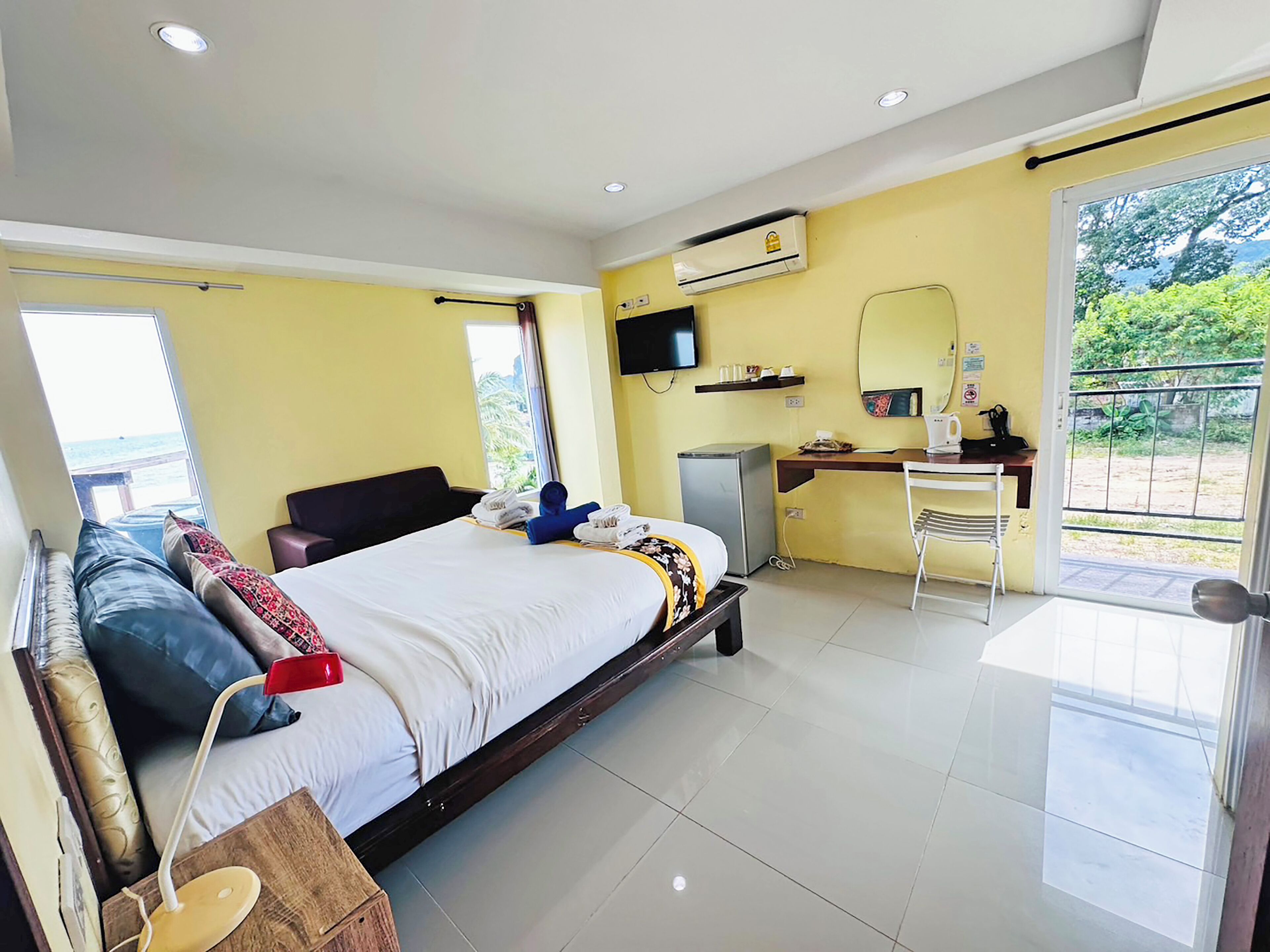 A hotel room with a bed, a desk, a chair, an air conditioner, a TV, and a view of the outdoors.