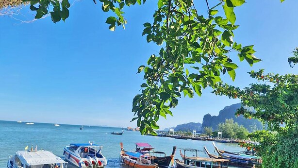 A coastal scene with boats docked at a pier, surrounded by lush greenery and clear blue skies. - Anyavee Chom By The Sea (Krabi)