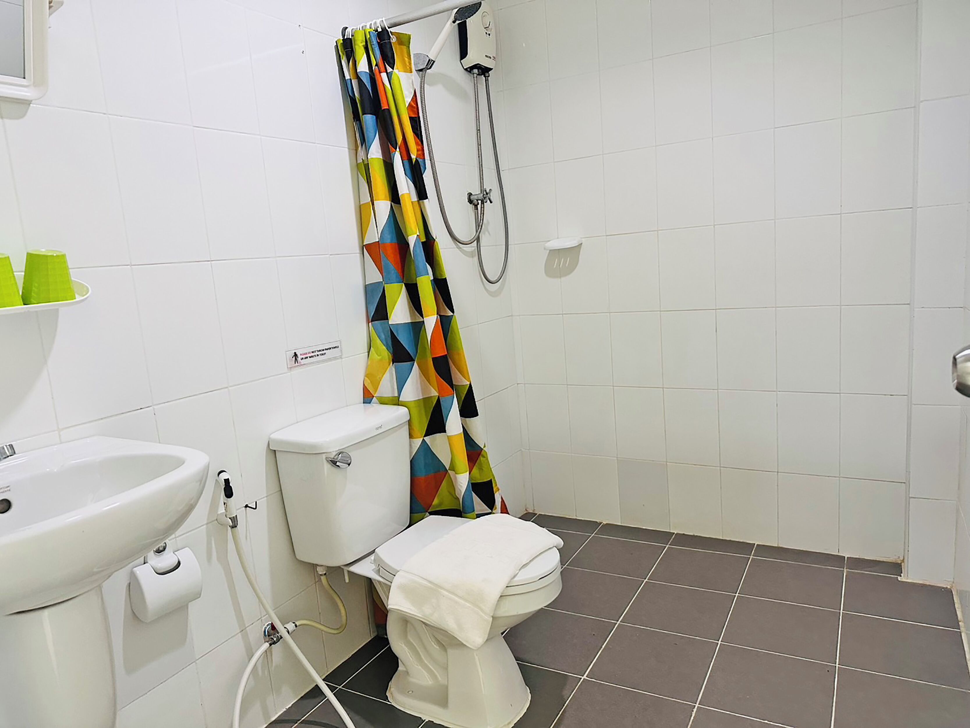 Une salle de bain équipée de toilettes, d’un lavabo et d’une douche agrémentée d’un rideau de douche aux motifs géométriques et aux couleurs vives.