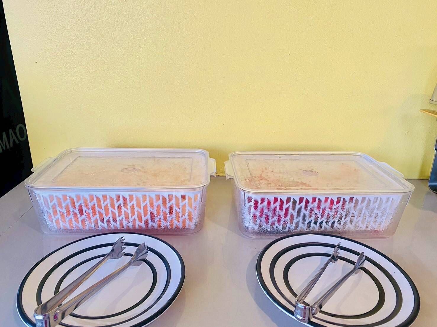 Two plastic storage containers with lids on a table against a yellow wall.