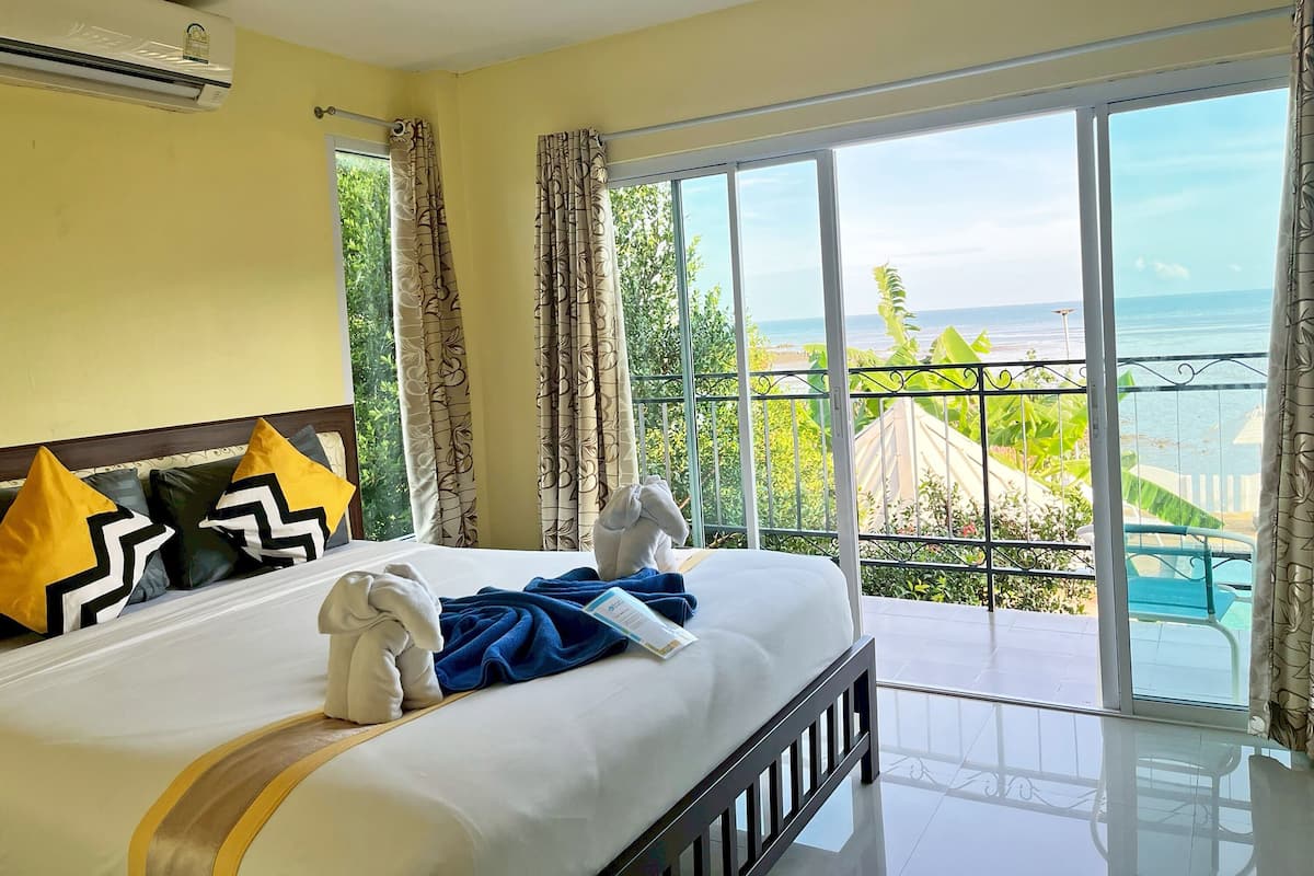 Habitación de hotel con una cama grande, un balcón con vista al mar y un aire acondicionado en la pared.