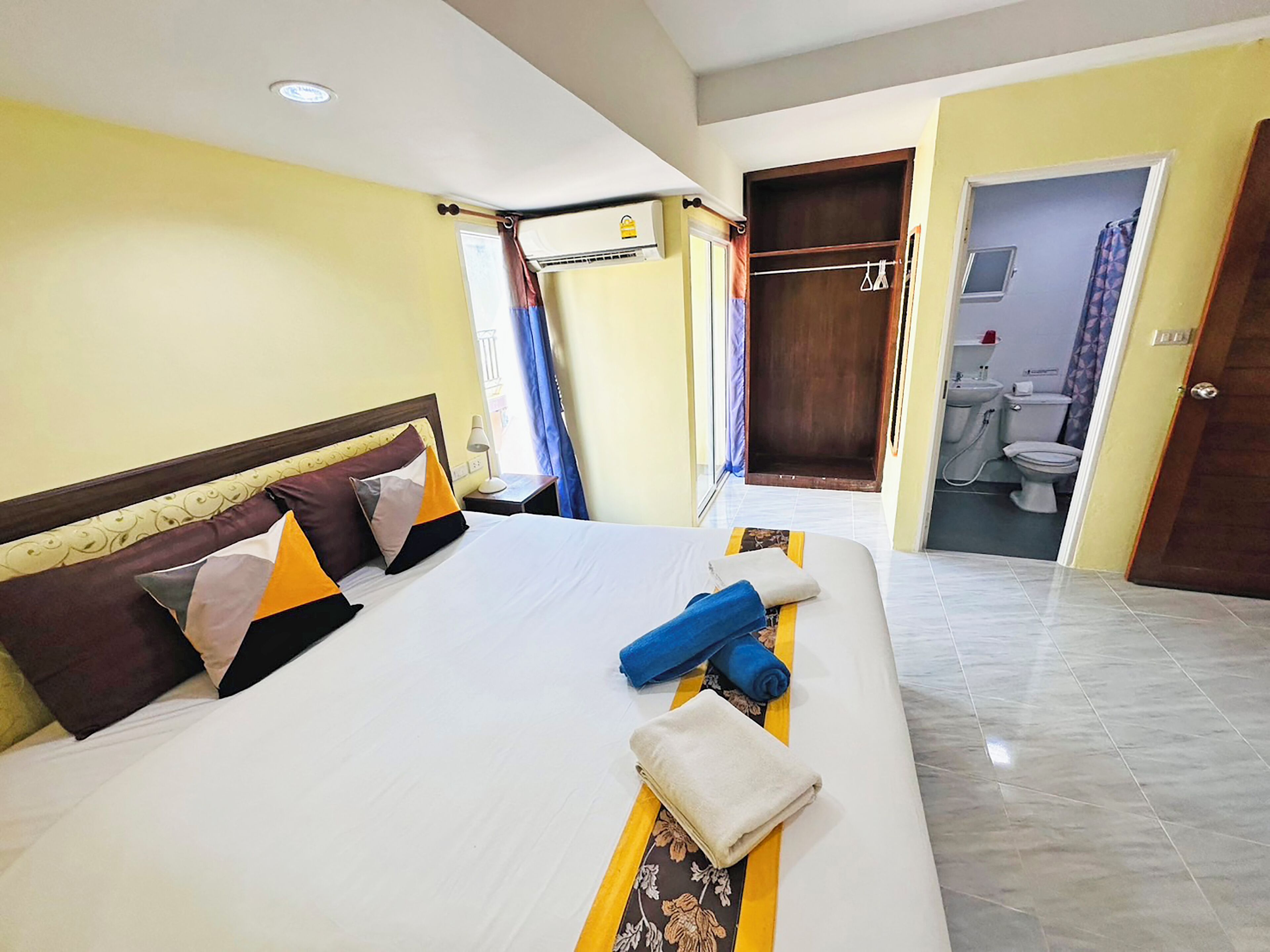 Quarto de hotel com uma cama grande, banheiro com vaso sanitário e pia, e um guarda-roupa.
