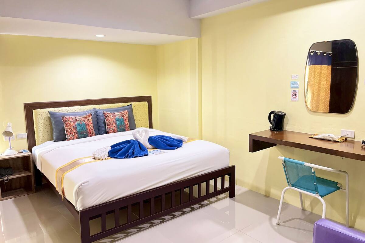 Una habitación de hotel con cama, escritorio, silla, espejo y cafetera.