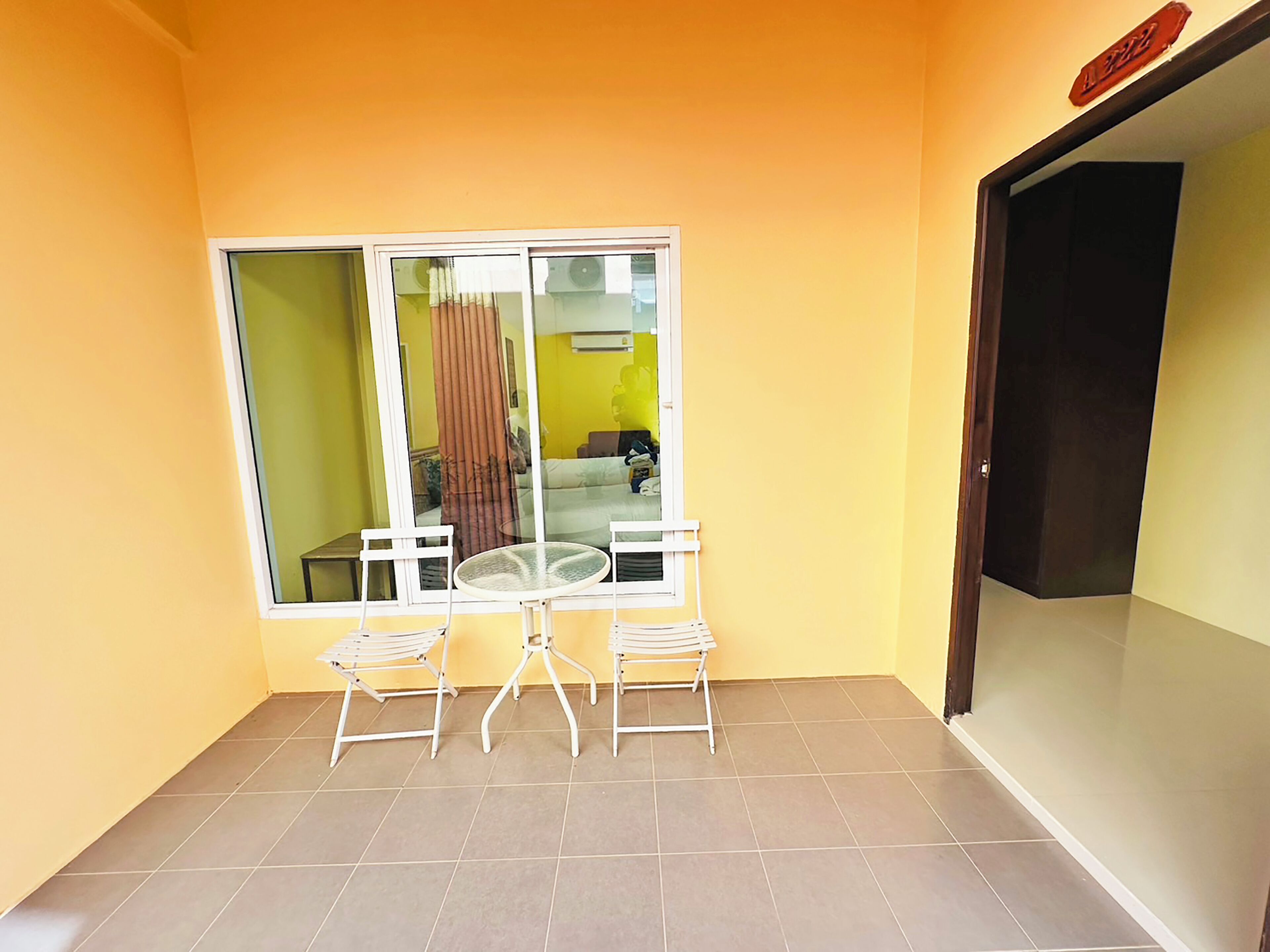 Un petit balcon avec une porte vitrée, deux chaises blanches et une table ronde.