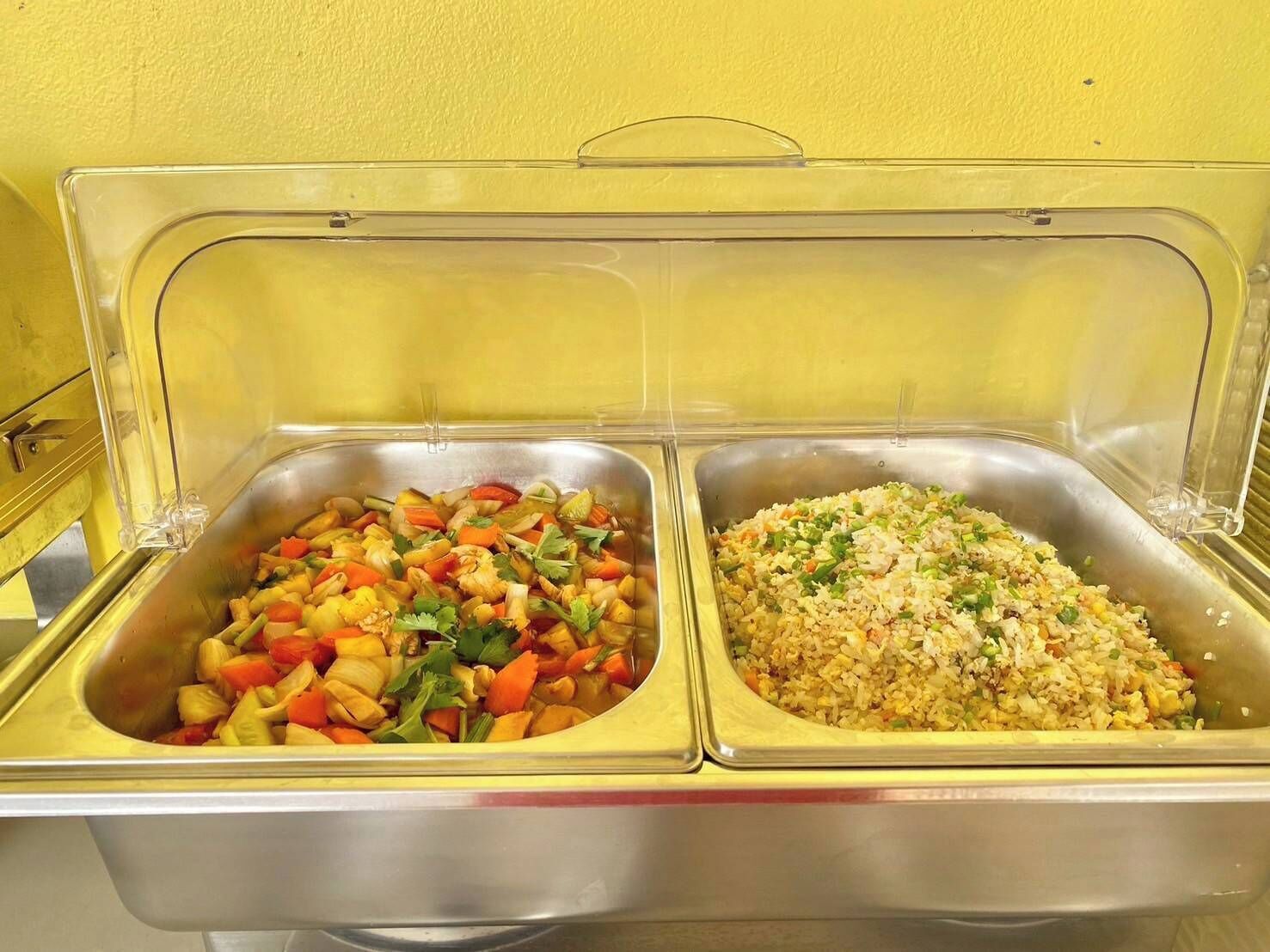 Ein Buffet mit zwei Speisenauslagen, eine mit Gemüsepfanne und die andere mit gebratenem Reis.