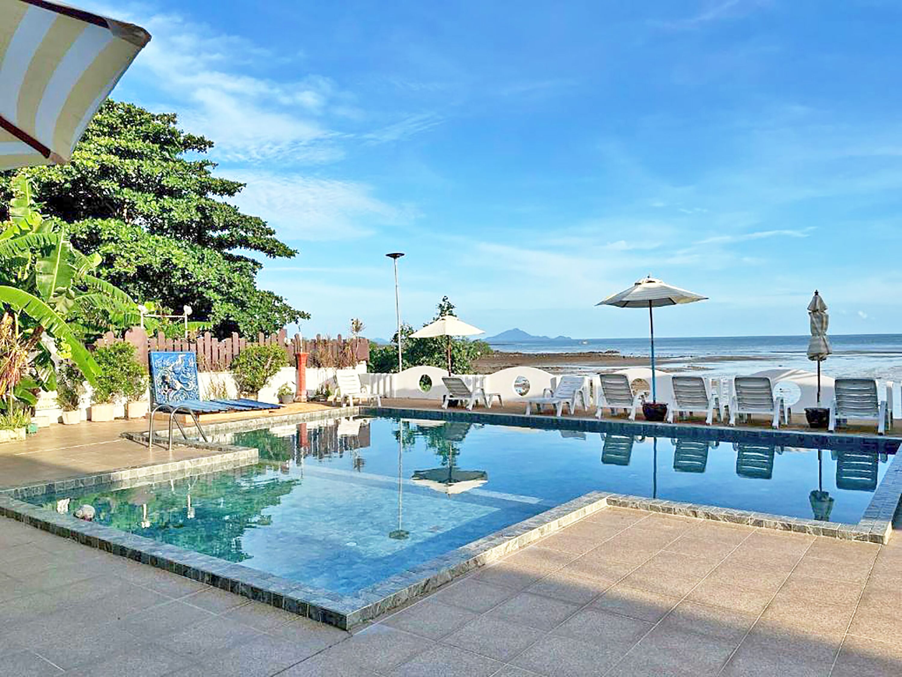 A swimming pool with lounge chairs and umbrellas, surrounded by greenery and a view of the ocean.