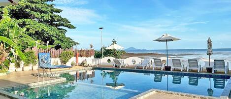 A swimming pool with lounge chairs and umbrellas, surrounded by greenery and a view of the ocean.