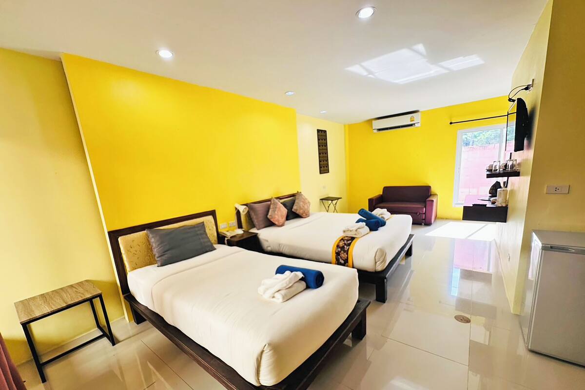 Habitación de hotel con dos camas, una mesita, un sofá, un televisor y un refrigerador.