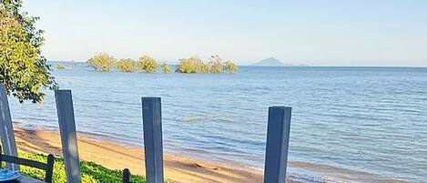 Mesa dispuesta para una comida con mariscos, verduras y salsas, con vista a una playa y al agua.