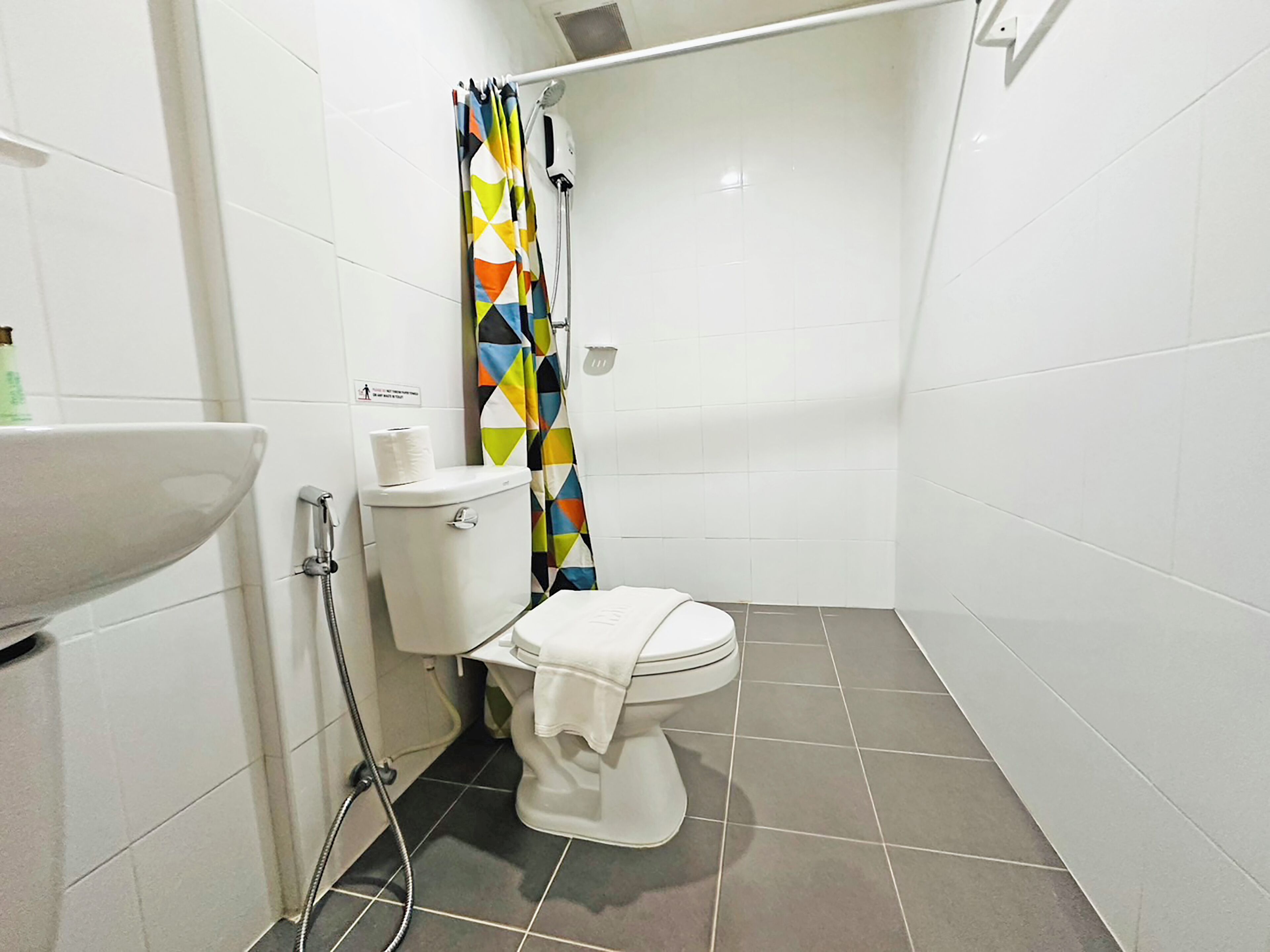 A small, modern bathroom with a toilet, a shower with a colorful curtain, and a white sink.