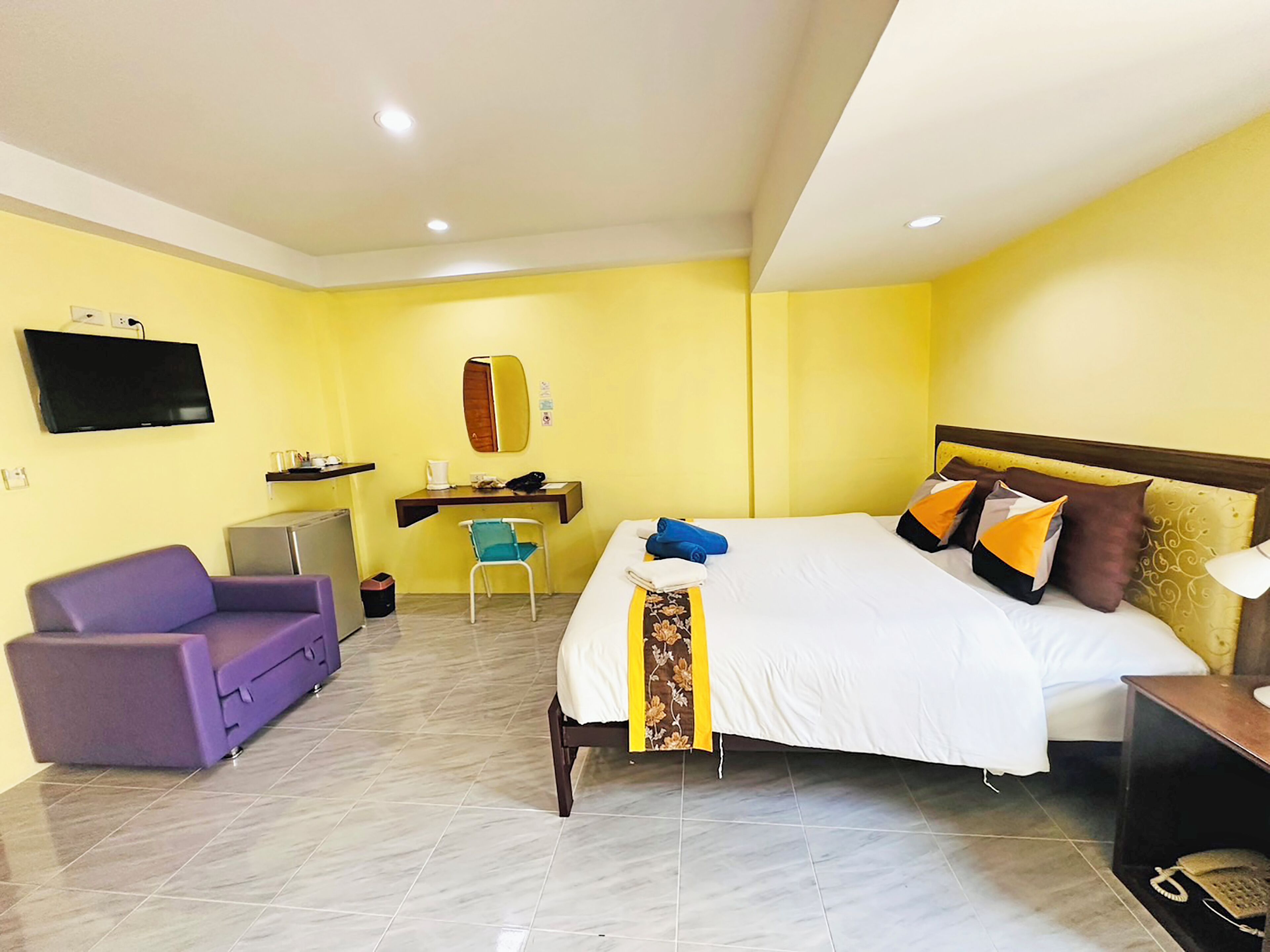 Une chambre d’hôtel avec un lit, un bureau, une chaise, une télévision et un canapé violet.