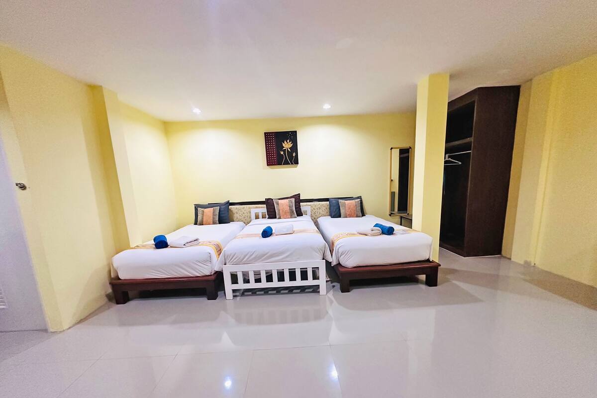 Una habitación de hotel con tres camas, un cabecero blanco y un espejo grande en la pared.