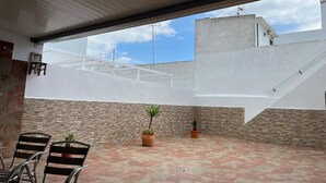 Un patio al aire libre con suelo de baldosas, algunas sillas y plantas en macetas.