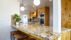 Eine Küche mit Holzschränken, Granit-Arbeitsplatten, einer zentralen Kochinsel mit Barhockern und modernen Geräten, darunter eine Mikrowelle und ein Backofen.