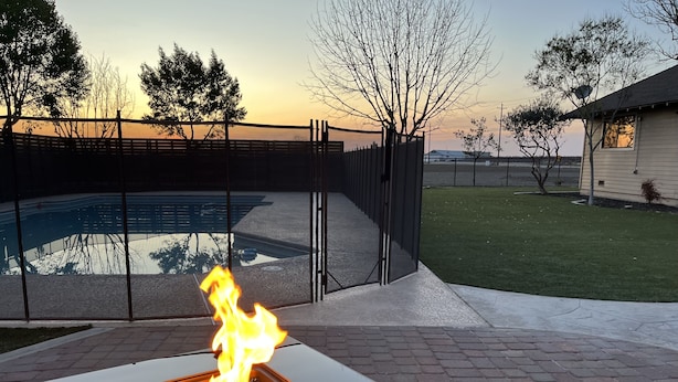 Ein quadratisches Außenfeuer mit einem Pool im Hintergrund.