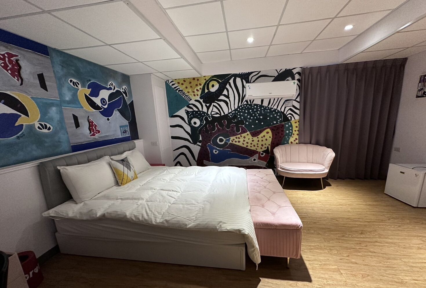 Une chambre moderne avec un grand lit, un petit coin salon et des œuvres d’art murales abstraites et colorées.