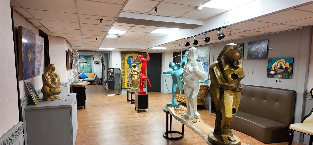 A gallery with various sculptures on pedestals, a wooden floor, and a brown sofa in the foreground.