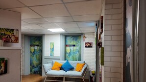 A hallway with a white couch with orange and blue cushions, a potted plant, and a wall with a painting and a sign that reads "ArtHome". - ARTHOME HOTEL (Kaohsiung)