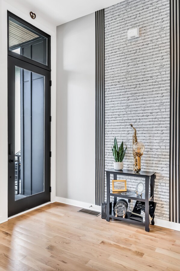 A modern interior with a black door, a wall with a musical note pattern, a wooden floor, and a console table with decorative items. - Studio C on Historic MusicRow
byGulch,12south,5MinBroadway (Nashville)