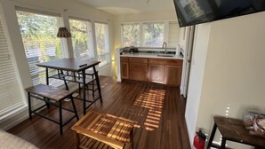 Eine geräumige Küche mit Holzausstattung, eine Essecke mit Tisch und Stühlen sowie große Fenster mit Jalousien.