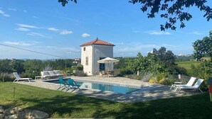 Un espace piscine avec des chaises longues, un petit bâtiment et une vue dégagée sur le paysage environnant.