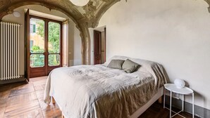 Une chambre avec un grand lit, une petite table de chevet et une vue sur l’extérieur par une porte.