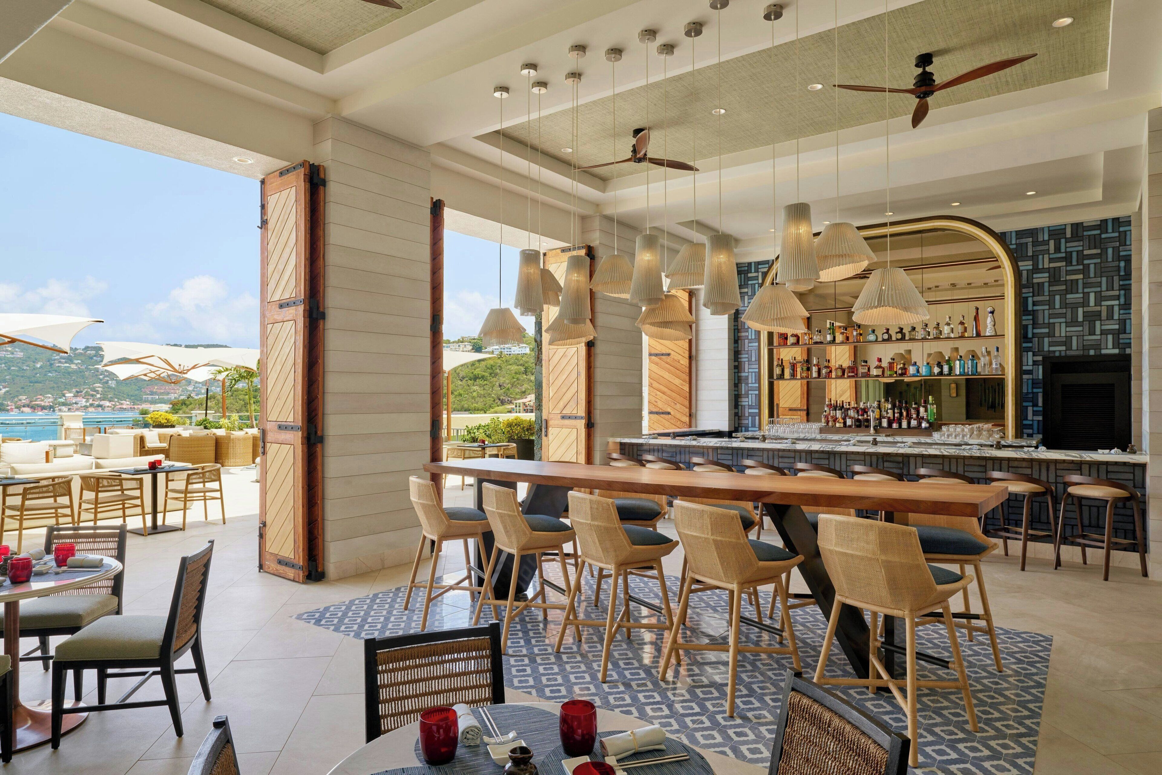 A bar area with a long counter, multiple hanging pendant lights, and a ceiling fan.