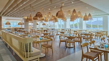 A spacious restaurant with high ceilings, wooden furniture, and large windows offering a view of the hills.