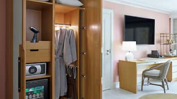 Camera d'albergo con un armadio in legno, una scrivania con sedia, una TV a schermo piatto e un piccolo frigorifero.