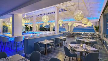 En modern restaurang med en bardel, bord och stolar, och med en vacker utsikt över havet genom stora fönster.