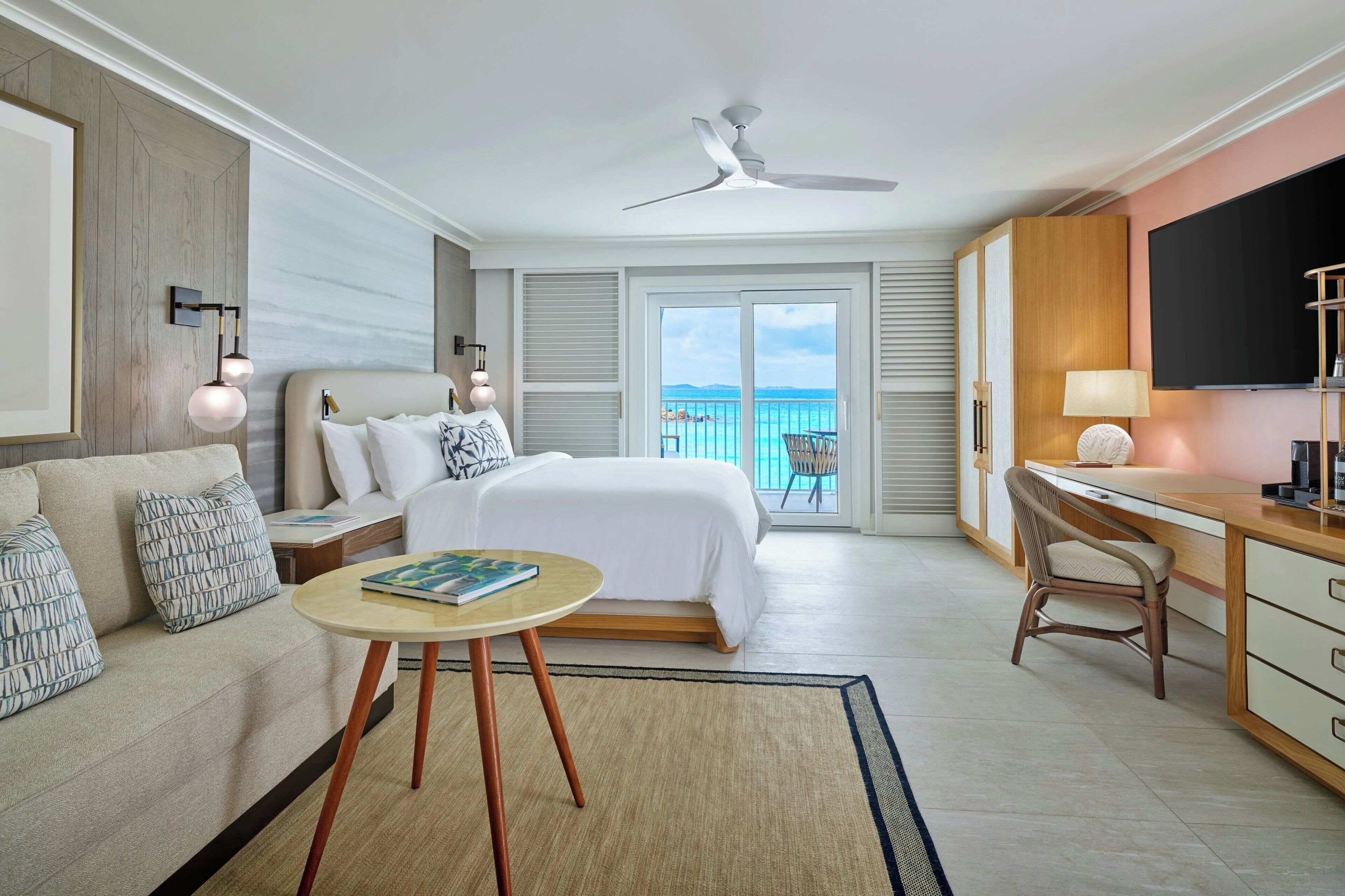 Habitación de hotel con cama, escritorio, silla, televisión y balcón con vistas.
