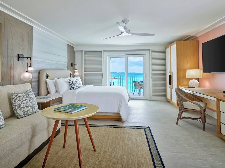 A hotel room with a bed, a desk, a chair, a TV, and a balcony with a view.