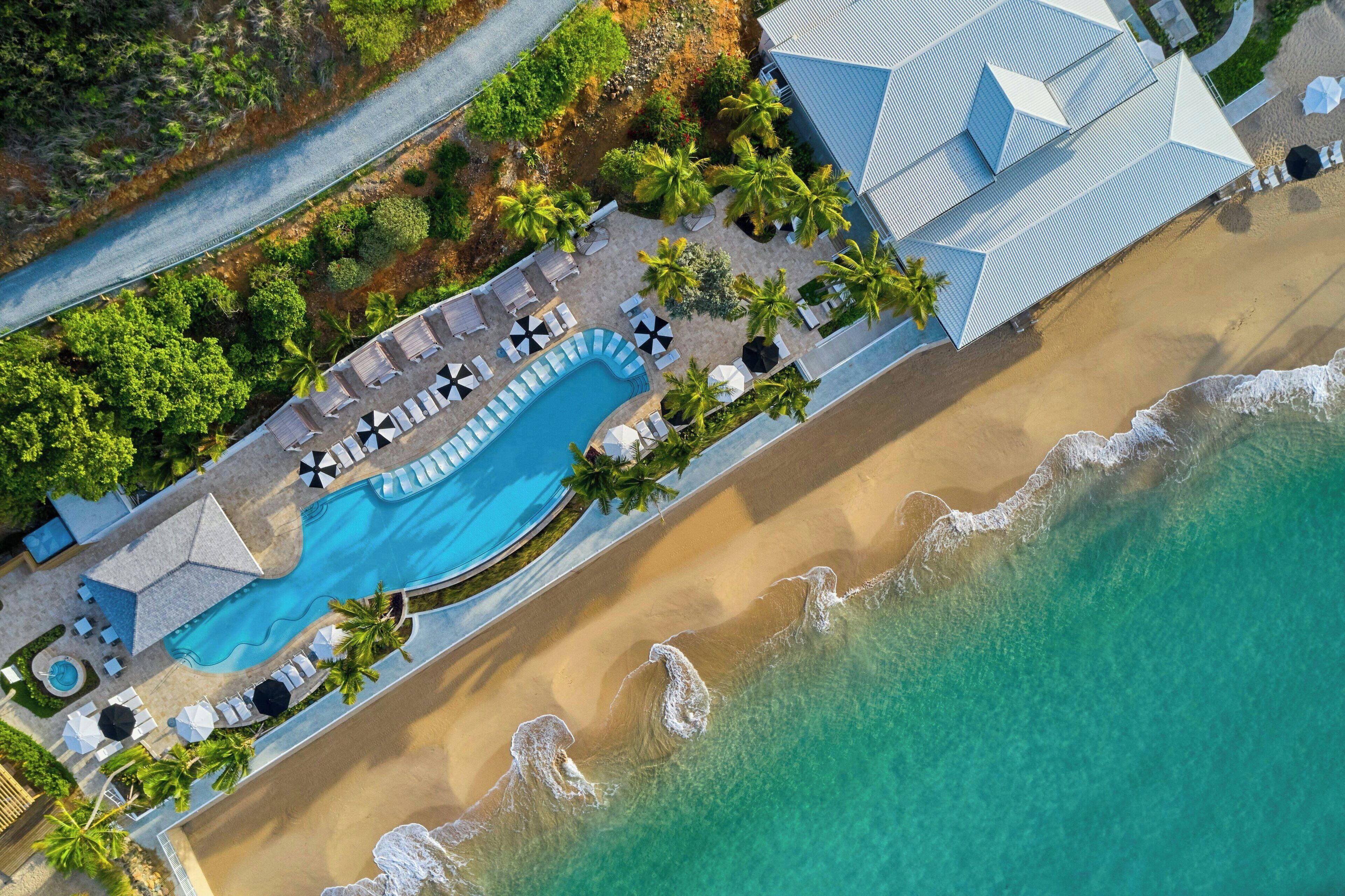 Vista aérea de un resort con piscina, playa y palmeras.