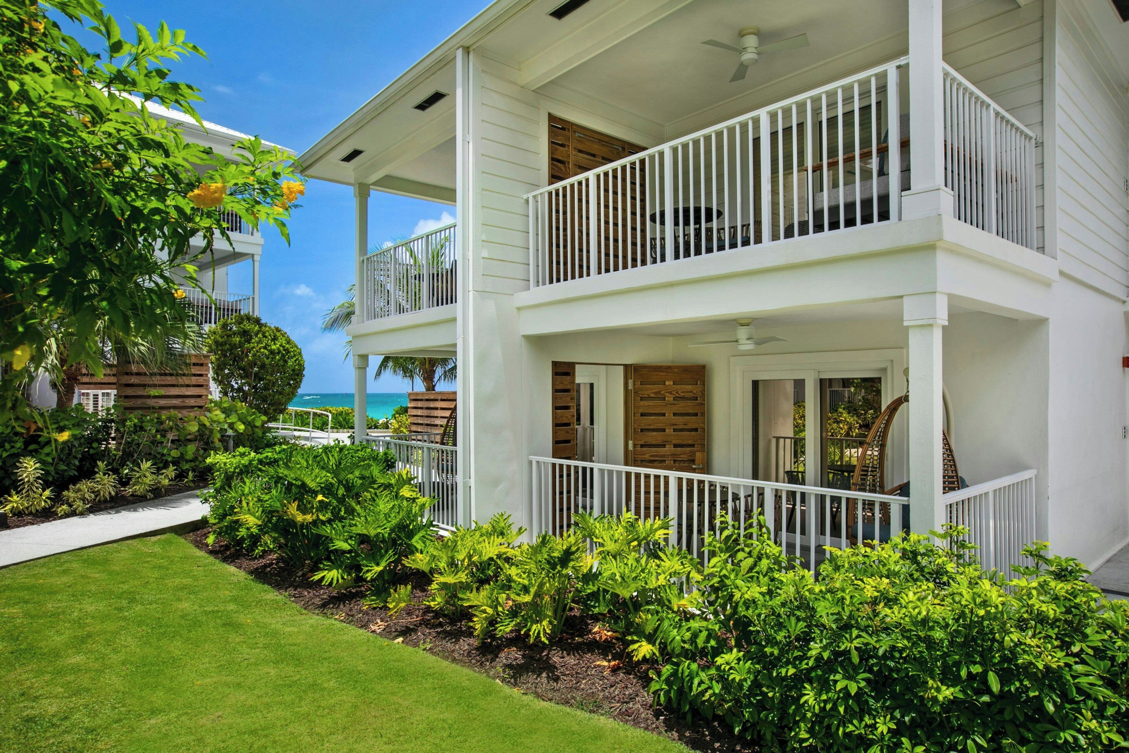 A two-story white building with balconies, a covered porch, and a well-maintained garden.