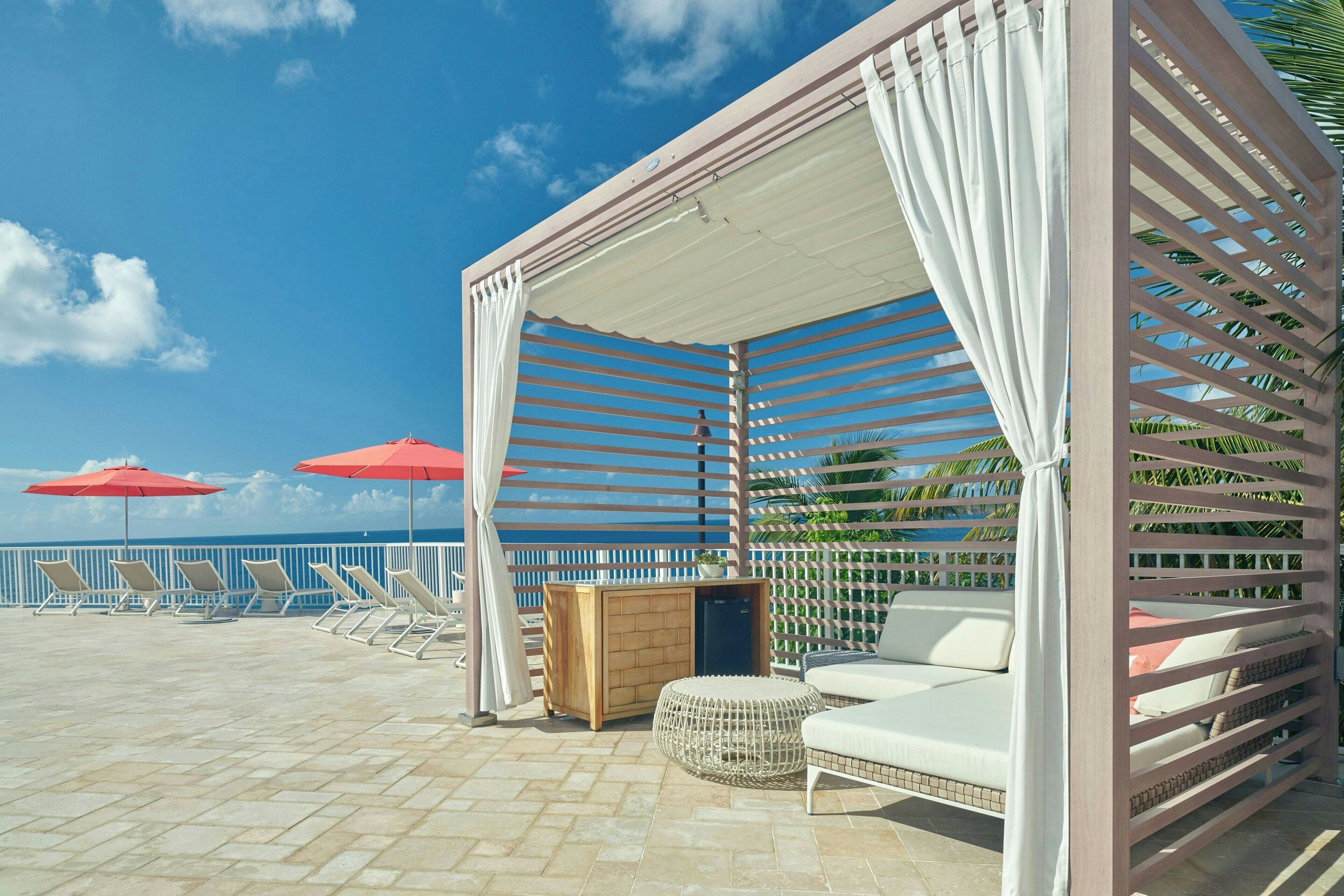 A rooftop terrace with lounge chairs, a wooden cabinet, and a cushioned seating area under a canopy.