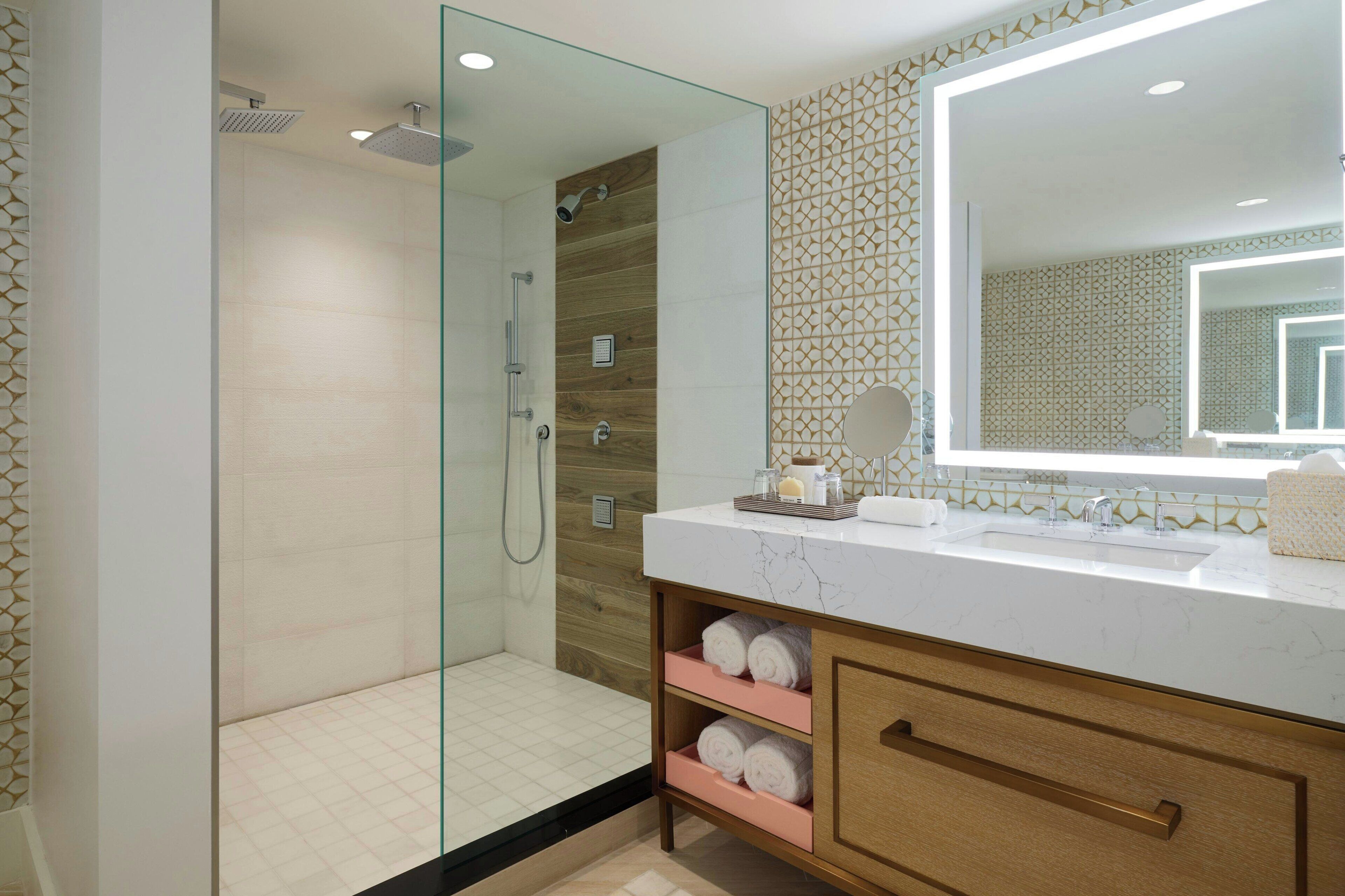 A modern bathroom with a glass-enclosed shower, a large mirror, and a marble countertop.