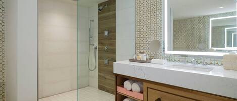 A modern bathroom with a glass-enclosed shower, a large mirror, and a marble countertop.