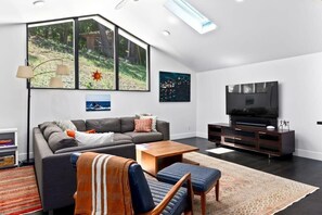 A modern living room with a large window, a flat-screen TV, and a cozy seating area.