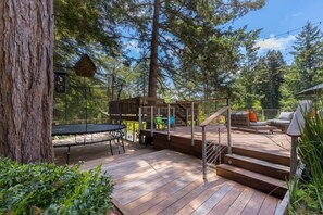 A wooden deck with a trampoline, outdoor seating, and a staircase leading to a deck area.