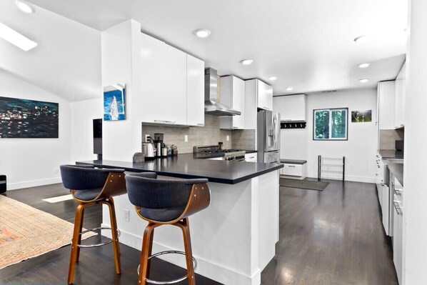 A modern kitchen with white cabinetry, a central island with bar stools, and recessed ceiling lighting.