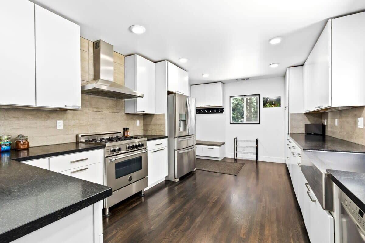 A modern kitchen with white cabinetry, stainless steel appliances, and a wooden floor.